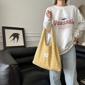 Detail of yellow gingham tote bag with woven brand label shown in minimalist room setting
