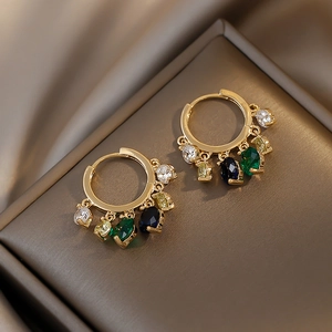 Detail of gold hoop earrings featuring five colorful teardrop gemstones on metal surface