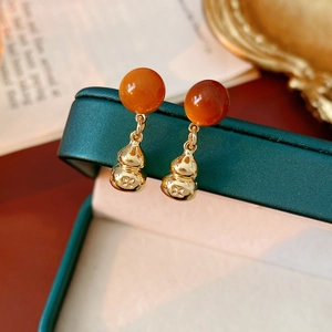 Macro shot of gold gourd drop earrings with orange beads on dark green jewelry box