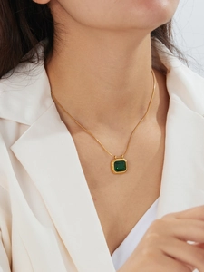 Close-up of a vintage gold snake chain necklace with a square emerald pendant on a model