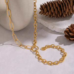 Détail d'un collier à maillons géométriques dorés sur une surface blanche avec pomme de pin