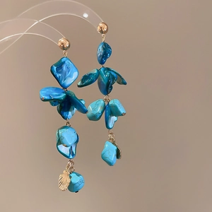 Detail of long drop earrings with blue shell pendants and gold chain on neutral background