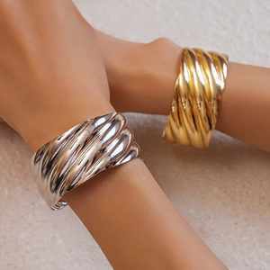 Detail of stacked gold and silver wave texture metal cuffs on model wrist with matte finish