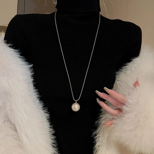 Gros plan d'un collier élégant plaqué or avec une grande perle sur un pull noir