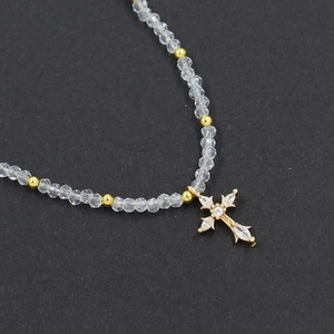 Macro detail of a golden cross pendant with zircons and faceted grey beads necklace