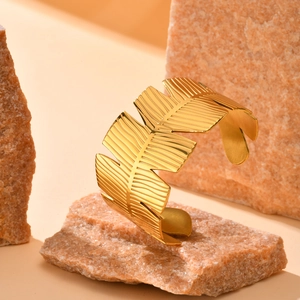 Detailed texture of a golden leaf-shaped open cuff bracelet resting on natural stones