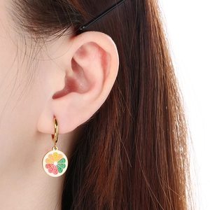 Gros plan d'un modèle portant des boucles d'oreilles dorées avec motif d'agrumes colorés
