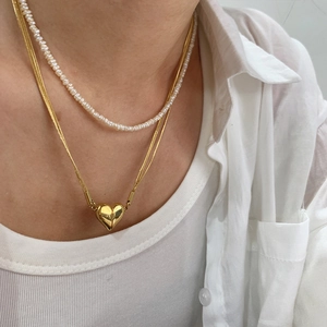 Detail of layered gold heart pendant and white pearl choker on a woman's neck