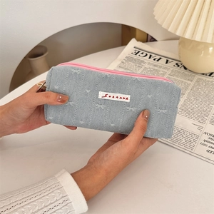 Detail view of denim pencil case with pink zipper and embroidered bow decoration