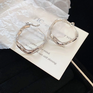 Macro detail of silver wavy multilayer irregular hoop earrings on a display card