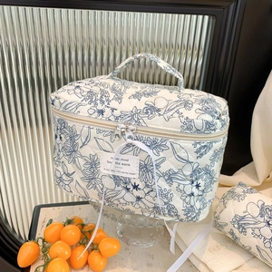 Detail of quilted cotton makeup bag with blue floral pattern and gold zipper with tag