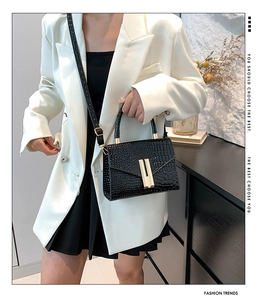 Chic black crocodile pattern handbag with gold clasp on model wearing a white suit