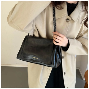 Detail shot of the black leather shoulder bag with a polished metal chain strap design