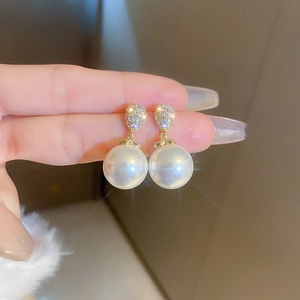Macro detail of tear-drop pearl earrings with sparkling zircon inlay and gold plating