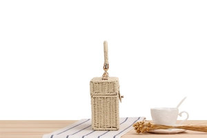 Detail of woven straw box bag with gold metal clasp on a wooden surface