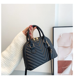 Detail of black shell-shaped handbag showing V-quilted stitching and gold metal zipper