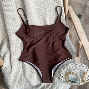 Dark coffee one-piece swimsuit with spaghetti straps and ruched detail on beach background
