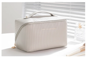 Close-up of cream vertical stripe pillow makeup bag with gold zipper and top handle