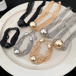 Close-up of multilayer metal chain necklaces and bracelets with large ball pendants in a bowl