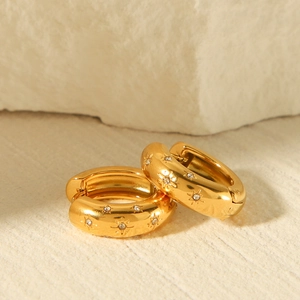 Detailed close-up of 18K gold earrings with starburst rhinestone inlay on beige stone