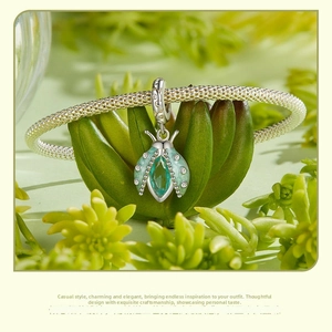 Detailed macro shot of a green beetle charm with enamel and stones on a silver bracelet