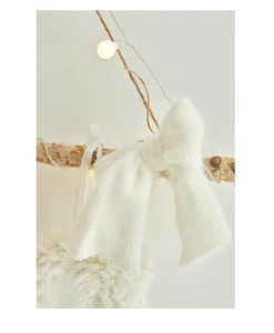 Close-up of a soft cream white knitted bow decoration hanging on a rustic wooden branch