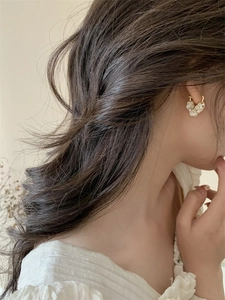 Close-up of a model wearing a gold heart earring with white pearl flower accents