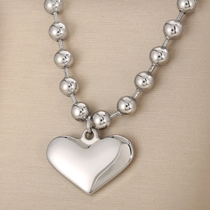 Detail shot of a silver heart pendant necklace with polished metal bead chain texture