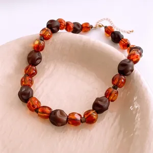 Collier rétro perles acryliques ambre et marron disposé sur un plateau en céramique