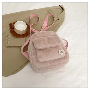 Detalle de mini mochila de felpa rosa sobre sábanas blancas con accesorios decorativos