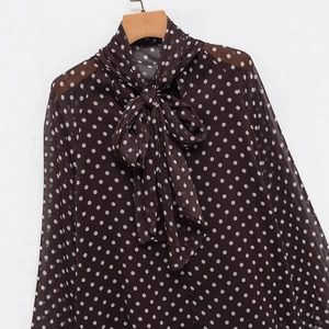 Brown polka dot chiffon blouse with a large bow tie neck design on a wooden hanger