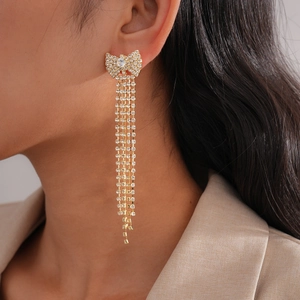 Dettaglio di orecchini a fiocco dorati con lunghe nappe di strass su modella