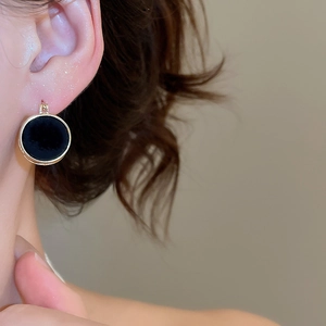 On-ear view of round black flocked pearl earrings with vintage gold metal accents