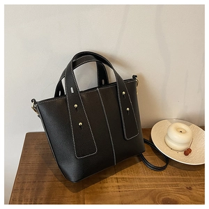 Detail of black lychee grain leather tote bag with contrast white stitching and gold studs