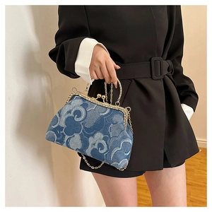 Blue denim handbag with cloud patterns, gold metal frame, and chain strap held by a model