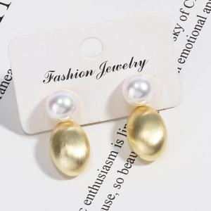 Macro shot of gold textured oval stud earrings with white pearls on a display card