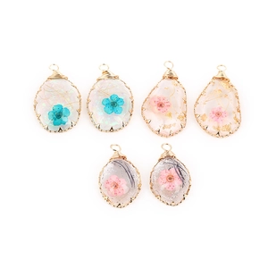 Handmade oval resin pendants with dried flowers and gold wire wrap details on white base