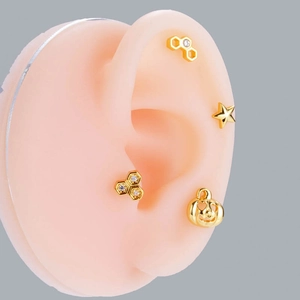 Close-up of gold steel ear studs featuring honeycomb, star, and pumpkin designs