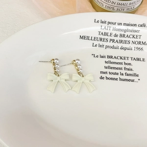 Elegant long bowknot earrings with cream pearls and gold finish on a ceramic plate