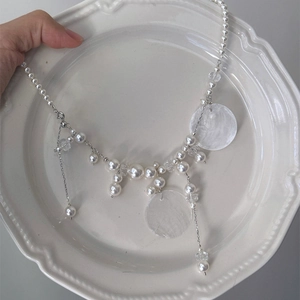 Detail of shell pearl tassel necklace held over a vintage white relief ceramic plate