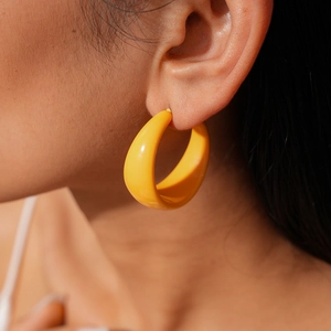 Side view of a female model wearing smooth yellow resin hoop earrings in warm light