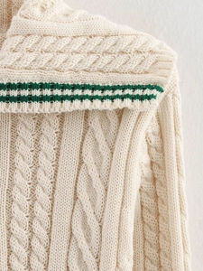 Close-up of beige knit sweater with cable texture and green striped collar detail