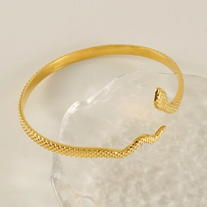 Minimalist 18k gold plated snake-shaped open bangle with textured scales on a glass base