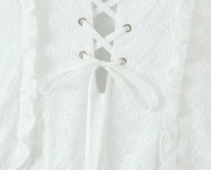 Detail eines weißen Baumwoll-Spitzenkleides mit Ösen und flachem Kordelzugverschluss