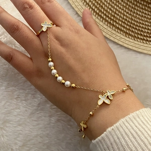 Dettaglio del bracciale ad anello dorato con perle e quadrifoglio sulla mano