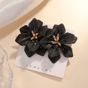 Elegant matte black flower earrings with gold center on a warm minimalist background