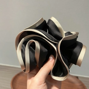 Close-up of black and beige two-tone satin scrunchie with layered ruffles and smooth texture