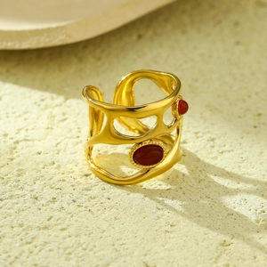Close-up of wide gold hollow ring with two red oval stones on a stone background