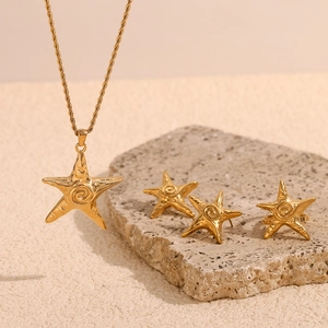 Close-up of gold starfish jewelry set including necklace, earrings, and ring on stone