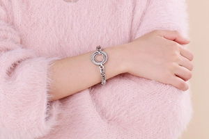 Détail du bracelet en argent à breloque cœur porté sur fond de tricot rose